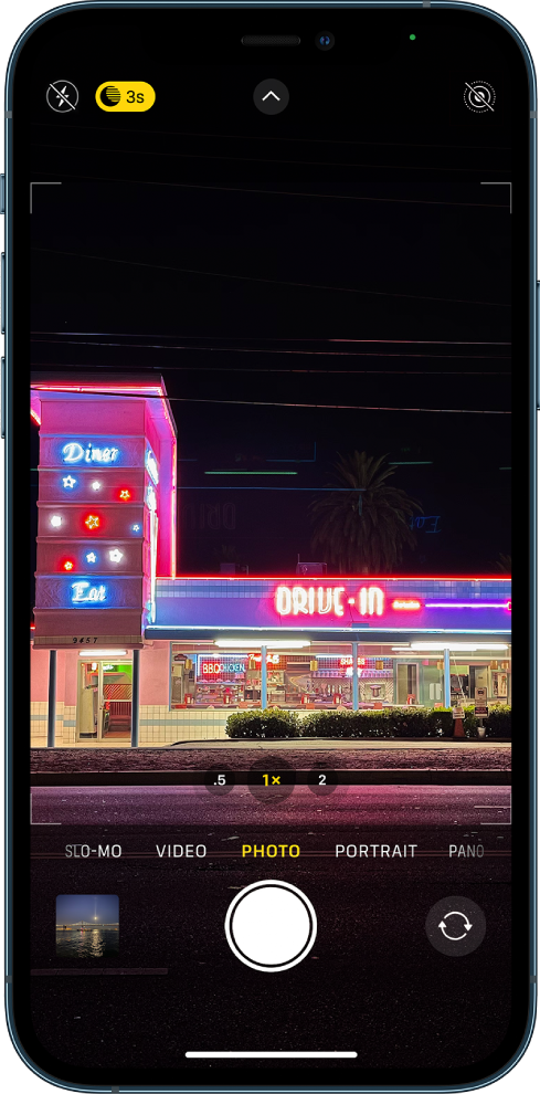 The Camera screen in Photo mode. Buttons for flash and Night mode appear in the top-left corner of the screen. The flash is turned off, and Night mode is on. The Camera Controls button is in top-center, and the Live Photo button is in the top-right corner. At the bottom of the screen are, from left to right, the Photo and Video Viewer button, the Take Picture button, and the Camera Chooser Back-Facing button.