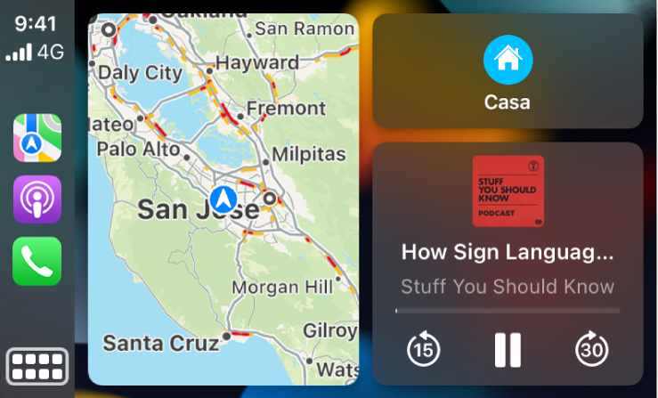 Panel de CarPlay con iconos para Mapas, Podcasts y Teléfono a la izquierda, el mapa de una ruta en coche en el centro y tres ítems apilados a la derecha. El ítem de arriba a la derecha muestra la navegación hasta Gasolineras y Aparcamiento. El ítem del centro a la derecha muestra los controles de reproducción de contenido. El ítem de abajo indica una cita próxima del calendario.