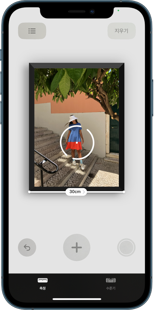 액자에 걸린 사진이 측정되어 하단 모서리에 너비가 표시됨. 오른쪽 하단 모서리에 있는 사진 찍기 버튼. 오른쪽 상단에 녹색 ‘사용 중인 카메라’ 표시기가 나타남.