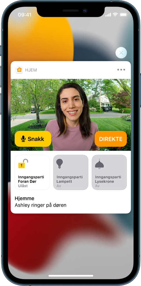 En varsling fra Hjem vises på iPhone-skjermen. Den viser et bilde av en person ved ytterdøren, med en Snakk-knapp til venstre. Nedenfor vises tilbehørsknapper for inngangspartiet og lysene i gangen. I teksten står det: «Ashley ringer på døren.» En Lukk-knapp vises øverst til høyre for varslingen.