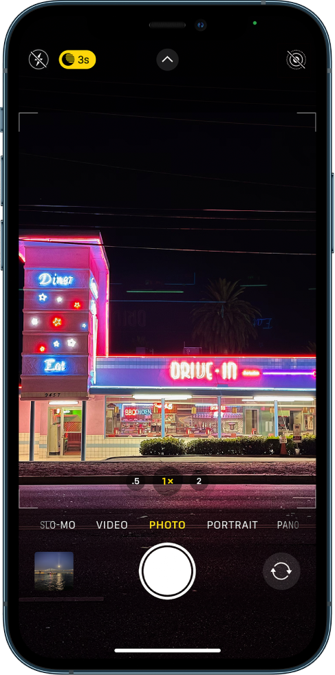 Zaslon Camera v načinu Photo. V zgornjem levem kotu zaslona sta prikazana gumba za bliskavico in način Night. Bliskavica je izklopljena in vklopljen je način Night. Gumb Camera Controls je v sredini zgoraj, gumb Live Photo pa je v zgornjem desnem kotu. Na dnu zaslona so z leve proti desni gumb Photo and Video Viewer, gumb Take Picture in gumb Camera Chooser Back-Facing.