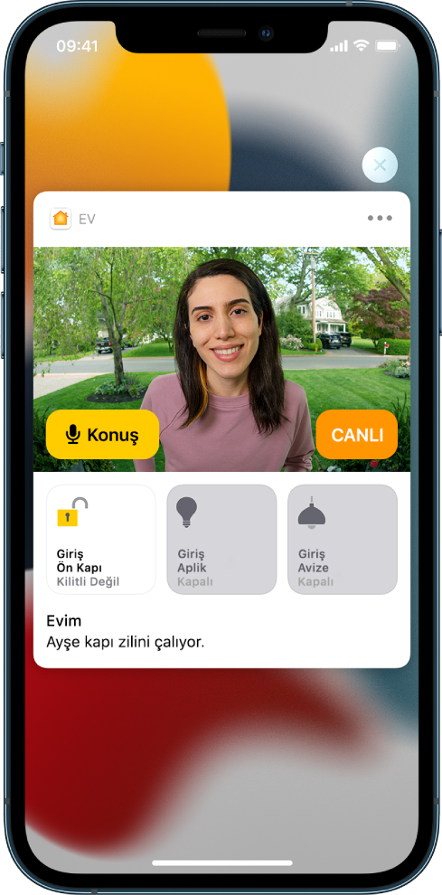 iPhone ekranında Ev uygulamasından bir bildirim var. Sol tarafta bir Konuş düğmesiyle ön kapıdaki bir kişinin resmi gösteriliyor. Alt tarafta ön kapı ve giriş ışıkları için aksesuar düğmeleri var. “Ayşe kapı zilini çalıyor” sözcükleri görünüyor. Bildirimin sağ üst tarafında Kapat düğmesi var.