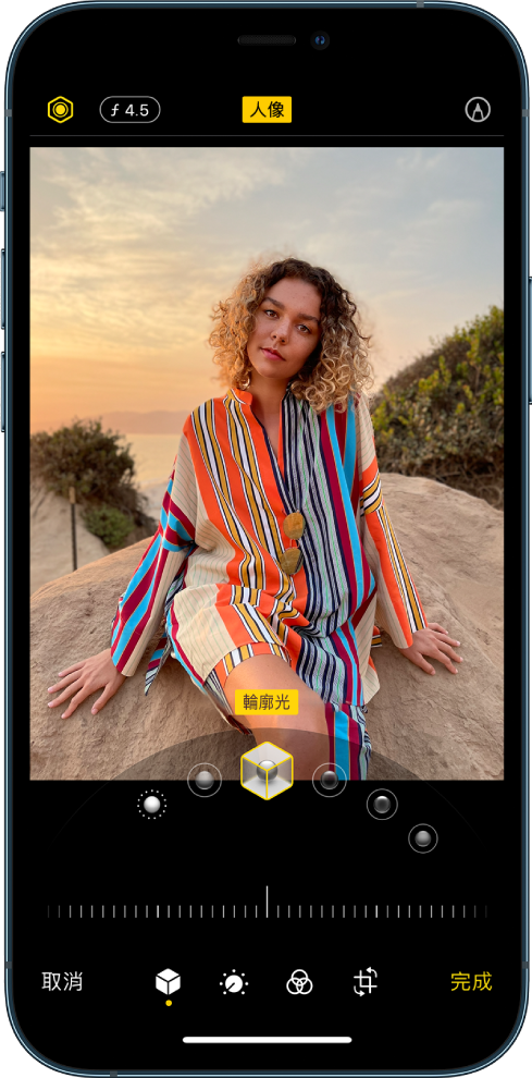 「人像」模式照片的「編輯」畫面。「光線強度」和「景深調整」按鈕位於螢幕左上角。螢幕上方中央顯示「人像」按鈕已開啟，右上角為「標示」按鈕。照片位於畫面中央，照片下方的滑桿用來選擇「人像光線效果」。其下方是用來調整值的滑桿。螢幕底部由左至右分別為「取消」、「人像」、「調整」、「濾鏡」、「裁切」和「完成」按鈕。