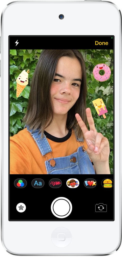 The Messages effects screen. The top of the screen shows the front camera frame. iMessage stickers are around the subject in the frame. Below the frame, from left to right, are the filters, text, shapes, Memoji, Emoji, and iMessage app buttons. At the bottom of the screen, from left to right, are the Effects, Shutter, and Camera Chooser Back Facing buttons.