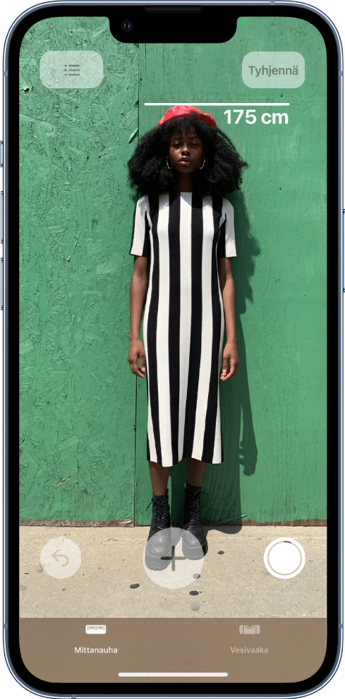Henkilön pituus mitataan ja lukema tulee näkyviin henkilön pään viereen. Ota kuva -painike on aktiivinen oikeassa alakulmassa, jotta voit ottaa kuvan mittauksesta. Vihreä kameran käytön merkki näkyy yläoikealla.
