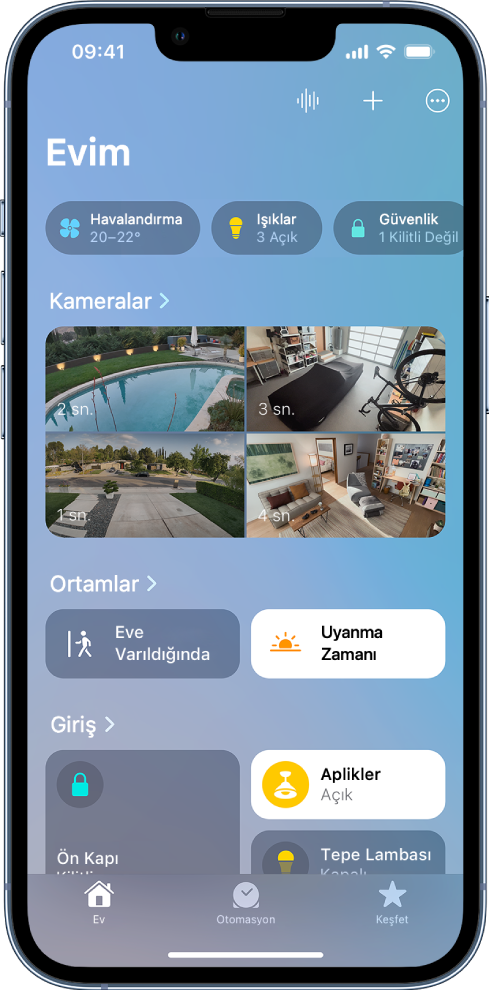 Ekranın en üstünde Kategoriler ile Ev sekmesi. Dört güvenlik kamerasından gelen görüntüler Kameralar başlığının altında görünüyor. Görüntülerde arka bahçe, garaj, ön bahçe ve salon gösteriliyor. Ekranın ortasında iki ortam ve onun altında bir oda ve aksesuarları görünüyor.