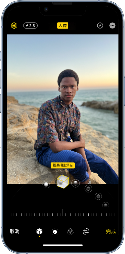 「人像」模式照片的「編輯」畫面。「光線強度」和「景深調整」按鈕位於螢幕左上角。螢幕上方中央顯示「人像」按鈕已開啟，右上角為「標示」按鈕。照片位於畫面中央，照片下方的滑桿用來選擇「人像光線效果」。其下方是用來調整值的滑桿。螢幕底部由左至右分別為「取消」、「人像」、「調整」、「濾鏡」、「裁切」和「完成」按鈕。