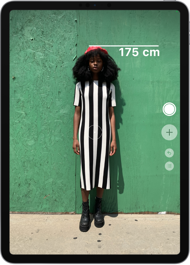 Измерване на височината на човек, като измерената стойност се показва на върха на главата на човека. Бутонът Снимане е активен вдясно, за да се направи снимка на измерването. Горе вдясно се появява зеленият индикатор Камерата се използва.