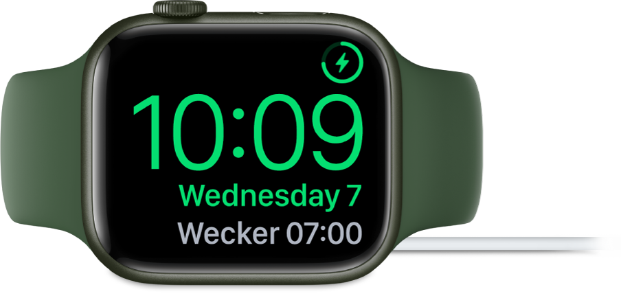 Eine auf die rechte Seite gedrehte Apple Watch, an die das Ladegerät angeschlossen ist und auf deren Display oben rechts das Ladesymbol, darunter die aktuelle Uhrzeit und die Uhrzeit für den nächsten Wecker angezeigt werden.