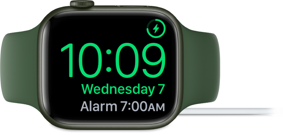 An Apple Watch placed on its side and connected to the charger, with the screen showing the charging symbol in the top-right corner, the current time below that, and the time of the next alarm.