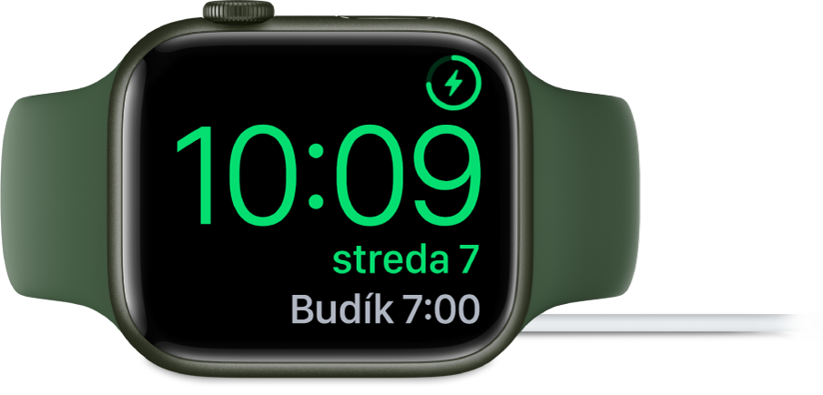 Hodinky Apple Watch otočené nabok a pripojené k nabíjačke. Na obrazovke je zobrazený symbol nabíjania v pravom hornom rohu, pod ním je aktuálny čas a nižšie je čas nasledovného budíka.