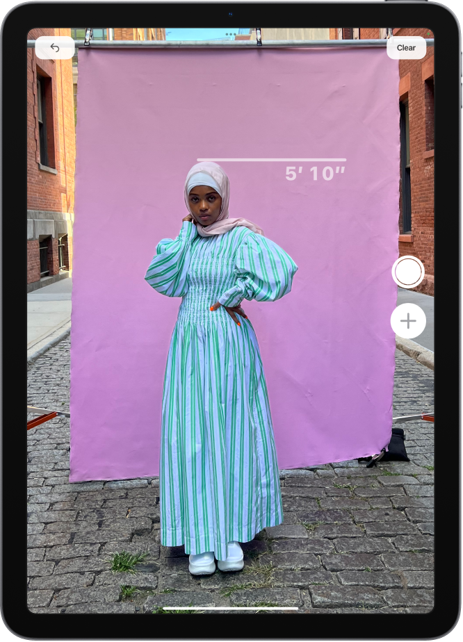 A person’s height is measured in the Measure app, with the height measurement showing at the top of the person’s head. The Take Picture button is active near the lower-right corner for taking a picture of the measurement. The green Camera In Use indicator appears at the top.