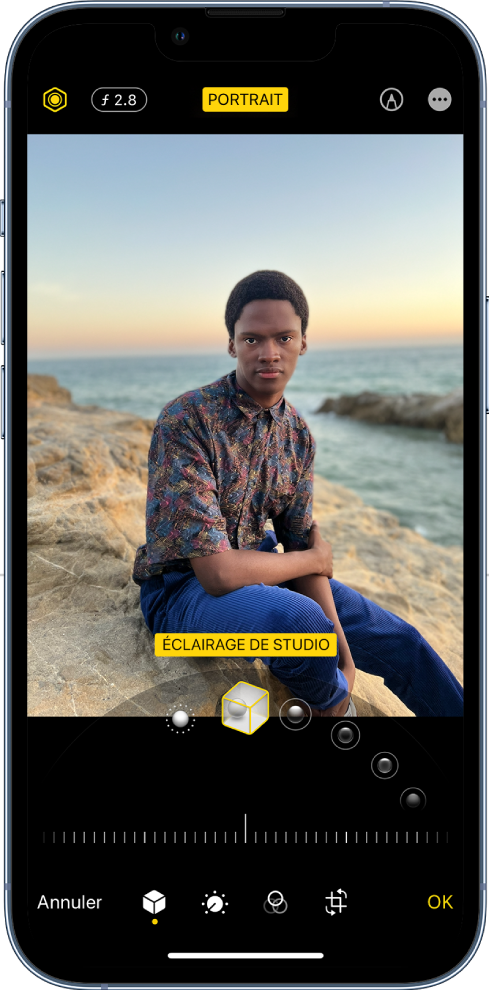 L’écran Modifier d’une photo prise en mode Portrait. En haut à gauche de l’écran se trouvent les boutons « Intensité de l’éclairage » et « Réglage de la profondeur ». En haut, au centre de l’écran, le bouton Portrait est activé. En haut à droite se trouve le bouton Annoter. La photo est au centre de l’écran ; sous celle-ci se trouve un curseur permettant de choisir l’effet d’éclairage de portrait. En dessous se trouve un curseur permettant d’ajuster la valeur de l’effet. En bas de l’écran, de gauche à droite, se trouvent les boutons Annuler, Portrait, Ajuster, Filtres, Recadrer et OK.