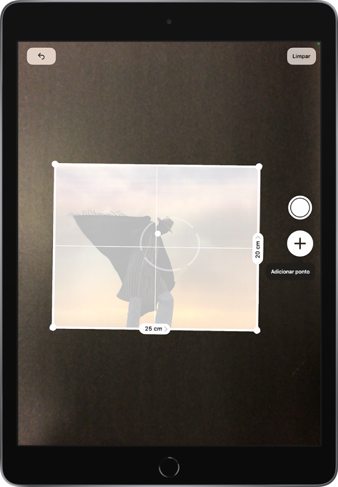 Uma fotografia em papel a ser medida, com as respetivas dimensões indicadas ao longo das extremidades direita e inferior. O botão “Tirar fotografia” encontra‑se sensivelmente a meio da extremidade direita. O indicador “Câmara em utilização” aparece na parte superior direita.