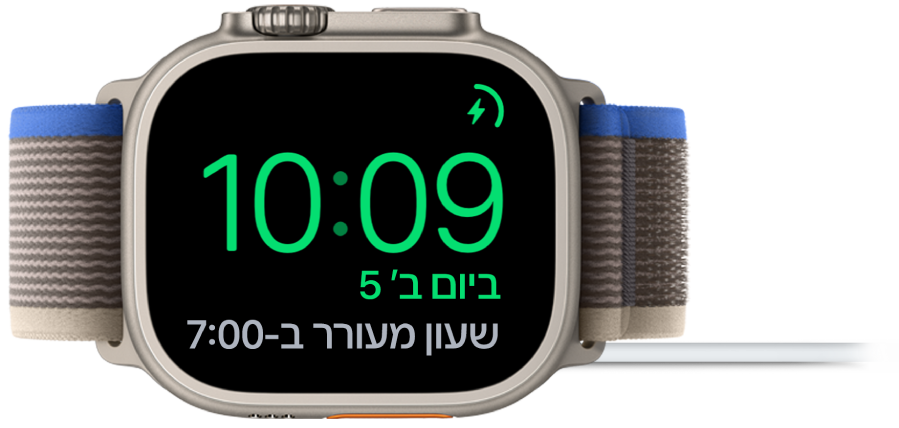 מכשיר Apple Watch מונח על צידו ומחובר למטען, כאשר המסך מציג את סמל הטעינה בפינה הימנית העליונה, את השעה הנוכחית מתחת לו ואת השעה הבאה אליה מכוון השעון המעורר.