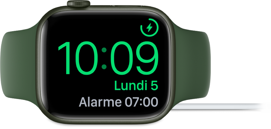Apple Watch placée sur le côté et connectée au chargeur, dont l’écran affiche le symbole de charge dans le coin supérieur droit, l’heure actuelle en dessous et l’heure de la prochaine alarme.