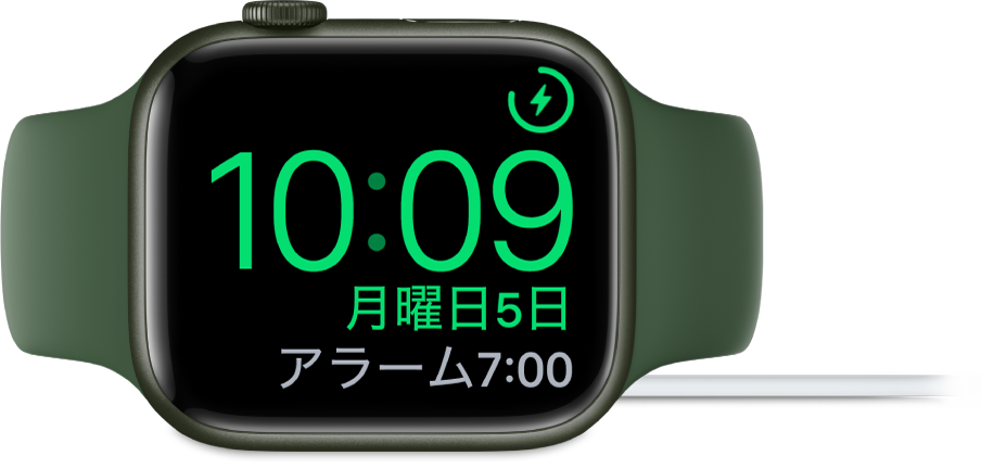 横向きに置かれ、充電器に接続されているApple Watch。画面には、右上隅に充電中のマーク、その下に現在時刻と、次のアラーム時刻が表示されています。