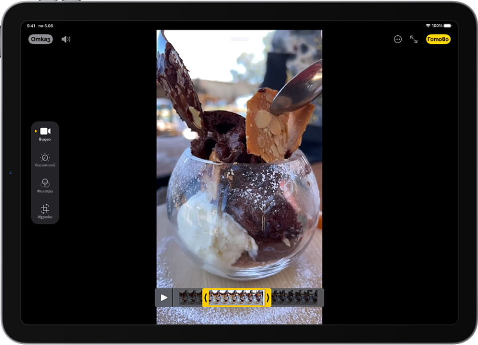 Екранът Редактиране в приложението Снимки с видео, което се възпроизвежда в средата. Прегледът на кадри за видеото е в долния край на видеото, а жълтият контур е около избраните кадри, които да се включат в изрязаното видео. Вляво на екрана са бутоните Видео, Настройка, Филтри и Изрязване; избран е бутон Видео.