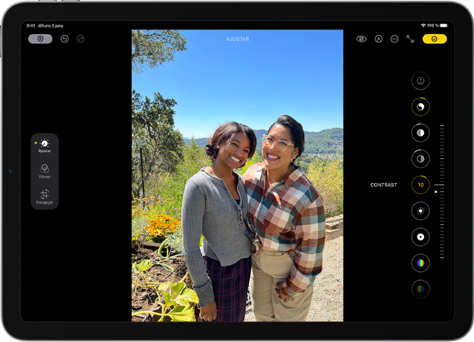La pantalla d’edició de l’app Fotos mostra una foto al centre. A l’esquerra de la foto hi ha els botons “Ajustar”, “Filtres” i “Escapçar”. El botó “Ajustar” està seleccionat. A la dreta de la foto hi ha els botons d’efectes d’edició i un regulador per ajustar el nivell de cada efecte.