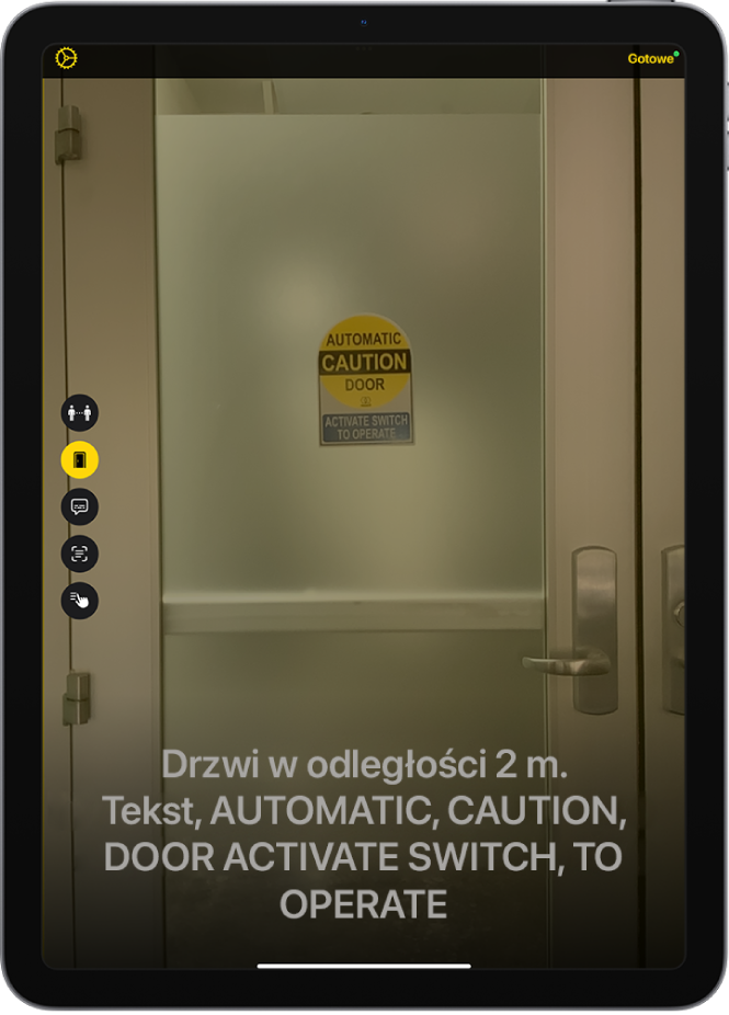 Ekran aplikacji Lupa w trybie wykrywania, wyświetlający drzwi. Na dole ekranu widoczny jest opis odległości, w jakiej znajdują się drzwi, a także tekst na drzwiach.