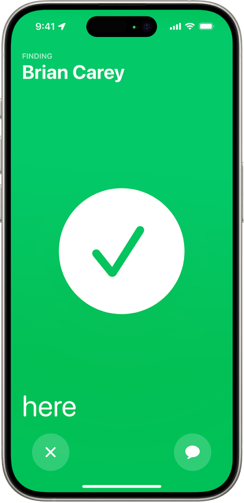 The iPhone screen is green with a big checkmark in the middle of it. The name of the person being located is in the top-left corner, and the word “here” is in the bottom-left corner, indicating that the meetup was successful.
