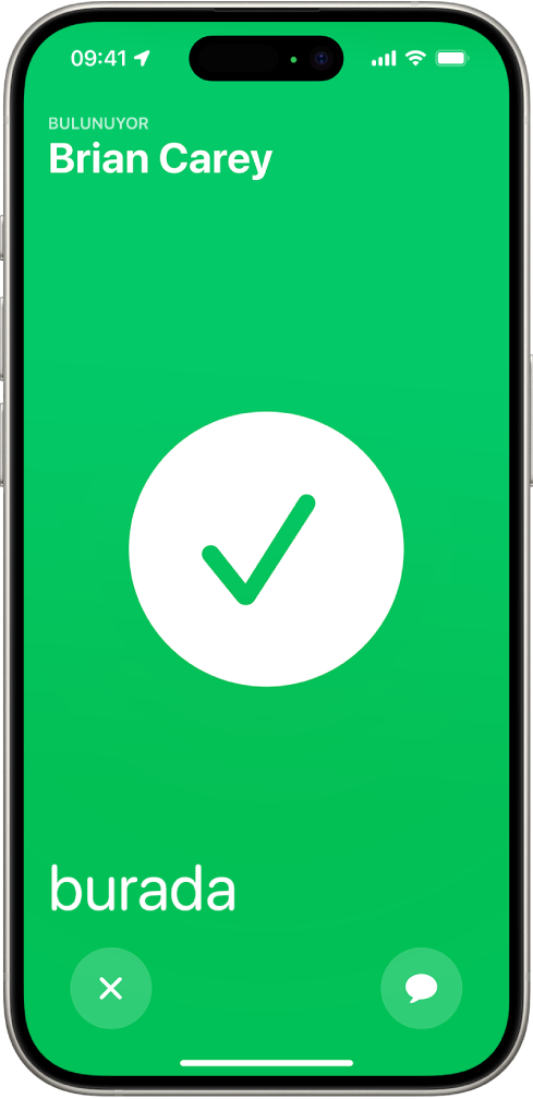 iPhone ekranı, ortasında büyük bir onay işareti ile yeşil renkte. Yeri bulunan kişinin adı sol üst köşede ve buluşmanın başarılı olduğunu belirten “burada” sözcüğü sol alt köşede.