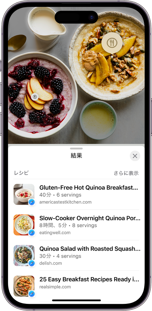 iPhoneの画面上部にさまざまな種類の食べ物の写真が表示されています。食べ物のうち2つの項目が「画像を調べる」によって特定され、片方の項目が選択されています。画面下部にはSafariのリンクが表示されています。「画像を調べる」によって特定された食べ物と同様の料理のレシピへのリンクです。