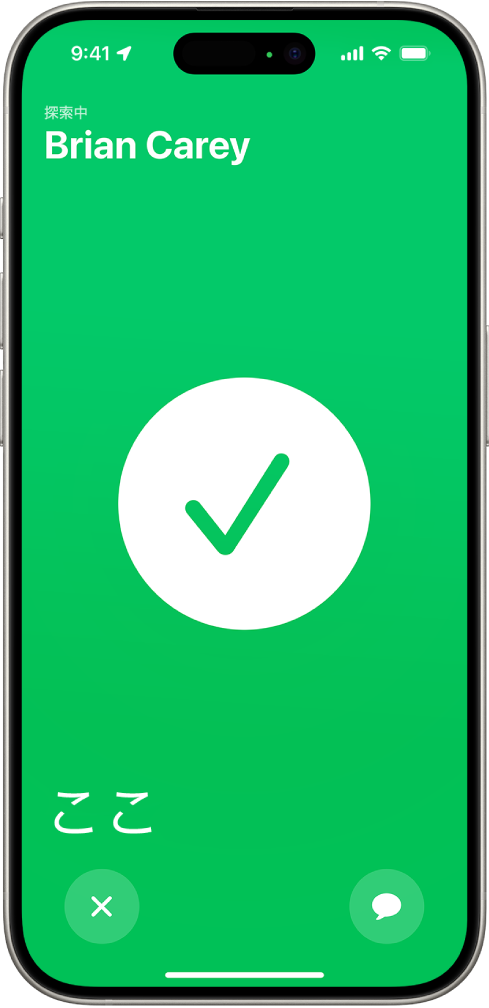iPhoneの画面が緑色になっていて、中央に大きなチェックマークが表示されています。探している人の名前が左上隅に、「ここ」という言葉が左下隅に表示され、無事に会えたことを示しています。