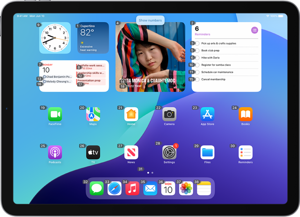 An iPad showing a number next to each item on the Home Screen. At the top of the screen, the Voice Control command “Show numbers” is displayed.