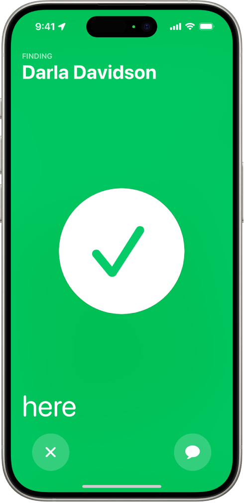 La pantalla del iPhone en color verde mostrando una gran marca de verificación en el centro. El nombre de la persona que se está localizando está en la esquina superior izquierda, y en la esquina inferior izquierda aparece la palabra “aquí”, indicando que se encontró correctamente.