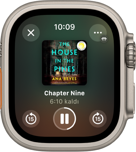 Sesli kitabın çalma ekranı. Kapat düğmesi sol üstte, Daha Fazla düğmesi sağ üstte, 15 saniye geriye atla düğmesi sol altta, Çal/Duraklat düğmesi alt ortada ve 15 saniye ileriye atla düğmesi sağ altta. Ortada kitap kapağı, bölüm numarası ve bölümde kalan süre bulunuyor.
