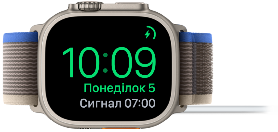 Apple Watch кладеться на бік і підключається до зарядного пристрою. На екрані відображається значок заряджання у верхньому правому куті, під ним — поточний час і час наступного будильника.