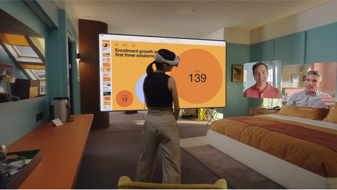 Une personne porte l’Apple Vision Pro et participe à un appel FaceTime. Les vignettes des autres participants à l’appel sont visibles à côté d’un écran partagé.