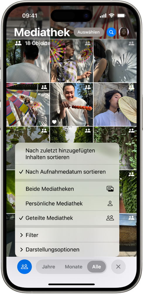 Eine geteilte iCloud-Fotomediathek in der App „Fotos“. Links unten ist die Taste „Geteilte Mediathek“ ausgewählt und in der Liste mit Mediatheksoptionen ist die Option „Geteilte Mediathek“ ausgewählt. Alle in der Mediathek angezeigten Fotos haben rechts oben das Symbol der geteilten Mediathek.