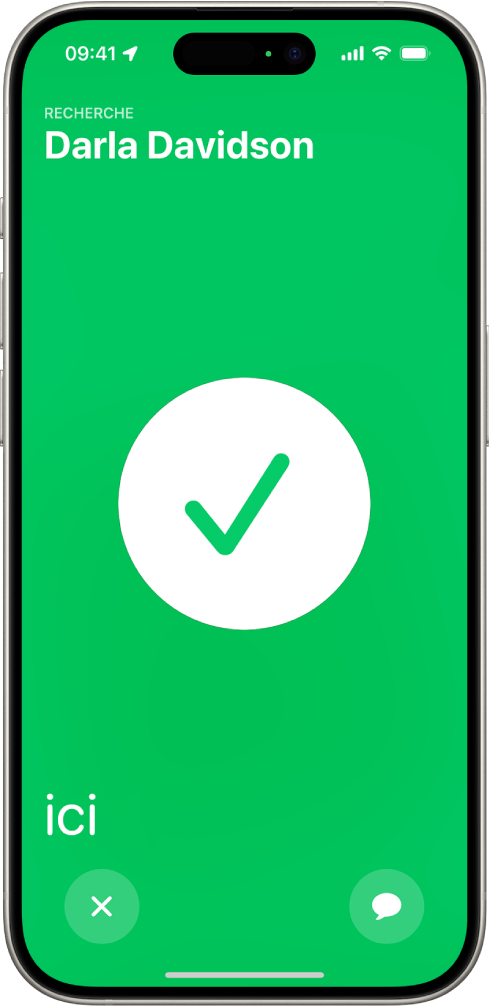 L’écran de l’iPhone est vert, avec une coche de grande taille au milieu. Le nom de la personne localisée apparaît en haut à gauche. Le mot « ici » se trouve en bas à gauche et indique que les deux personnes se sont trouvées.