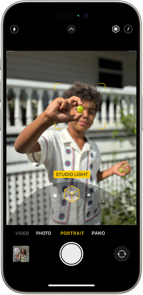 Екран Камери в режимі «Портрет»; у видошукачі об’єкт різкий, а тло розмите. Унизу кадру відкрито шкалу для вибору ефектів портретного освітлення. Вибрано «Студійне світло». Угорі зліва екрана — кнопка «Спалах», угорі по центру — кнопка «Елементи керування камери», а вгорі справа — кнопки для налаштування інтенсивності портретного освітлення та контролю глибини різкості. У нижній частині екрана зліва направо розташовані кнопки «Програма перегляду фото та відео», «Зробити знімок» і «Вибір задньої камери».