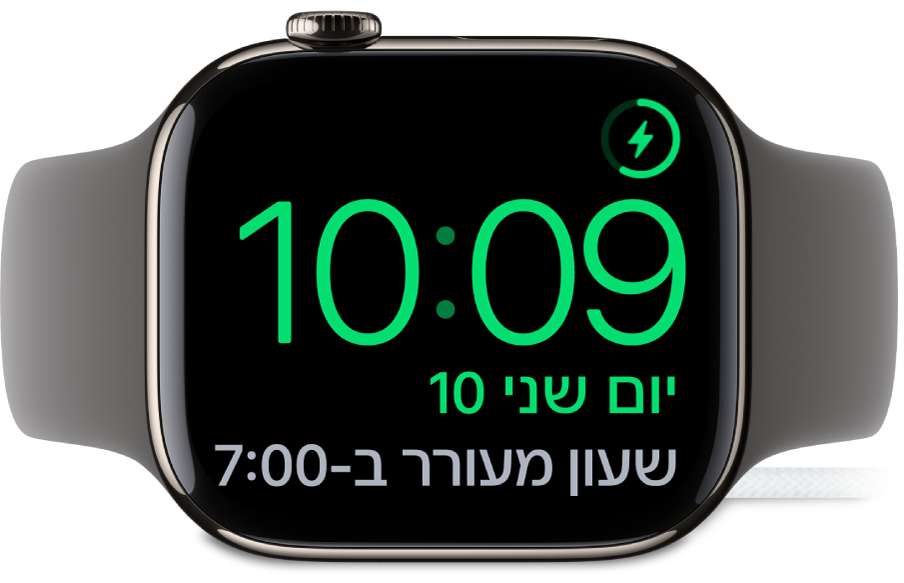 שעון Apple Watch מונח על צידו ומחובר למטען. המסך מציג את סמל הטעינה בפינה הימנית העליונה, ומתחתיו את השעה הנוכחית ואת השעה שבה יצלצל השעון המעורר הבאה.