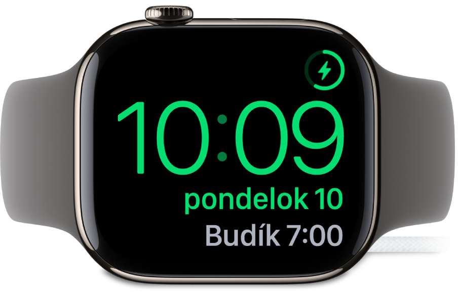 Hodinky Apple Watch otočené nabok a pripojené k nabíjačke. Na obrazovke je zobrazený symbol nabíjania v pravom hornom rohu, pod ním je aktuálny čas a nižšie je čas nasledovného budíka.