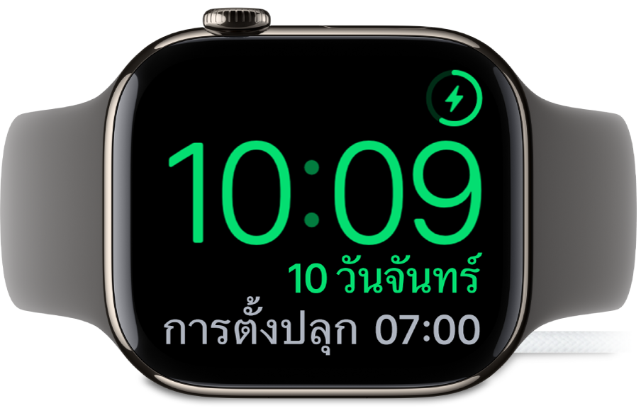 Apple Watch ที่วางตะแคง และเชื่อมต่ออยู่กับที่ชาร์จ โดยหน้าจอแสดงสัญลักษณ์การชาร์จตรงมุมขวาบนสุด เวลาปัจจุบันอยู่ด้านล่างสัญลักษณ์การชาร์จ และเวลาของการตั้งปลุกครั้งต่อไป