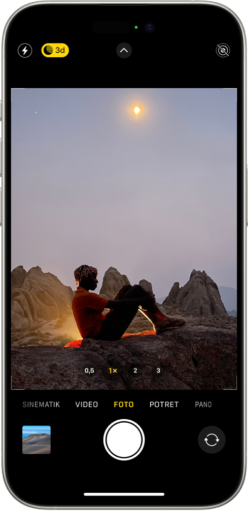 Layar Kamera dalam mode Foto. Dalam jendela bidik, terdapat pemandangan malam. Tombol untuk kilat dan mode Malam muncul di pojok kiri atas layar dan mode Malam menyala. Tombol Kontrol Kamera ada di tengah atas, dan tombol Live Photos terdapat di pojok kanan atas. Di bagian bawah layar terdapat, dari kiri ke kanan, tombol Penampil Foto dan Video, tombol Ambil Gambar, serta tombol Pemilih Kamera Belakang.