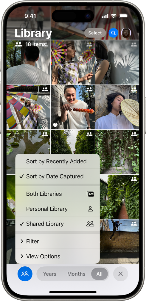 iCloud Shared Photo Library në aplikacionin Photos. Është zgjedhur butoni Shared Library në këndin e poshtëm majtas dhe është zgjedhur Shared Library në një listë të opsioneve të bibliotekës. Të gjitha fotot e shfaqura në bibliotekë kanë një stemë të përbashkët të bibliotekës në këndin e sipërm djathtas.