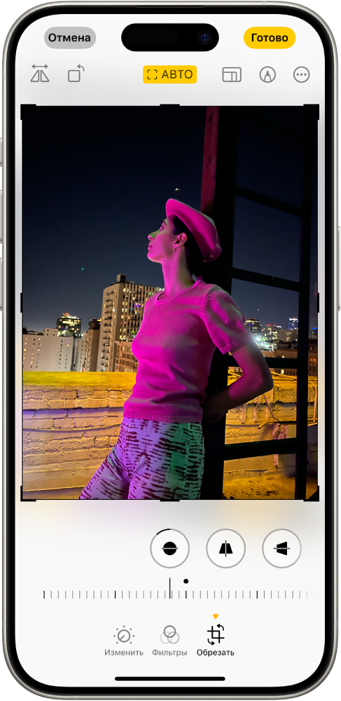 Экран редактирования с фотографией в центре. В нижней части экрана слева направо расположены кнопки «Настроить», «Фильтры» и «Обрезать». Выбрана кнопка «Обрезать», и над ней расположен бегунок для настройки улучшения геометрии снимка.