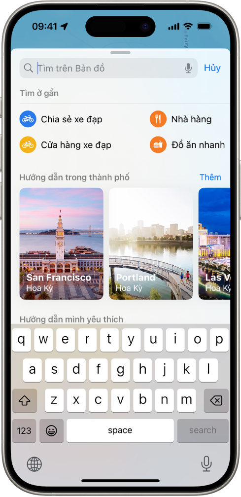 Ứng dụng Bản đồ đang hiển thị trường tìm kiếm, các danh mục cho dịch vụ ở gần và hướng dẫn thành phố. Phía dưới màn hình là bàn phím ảo của iPhone.