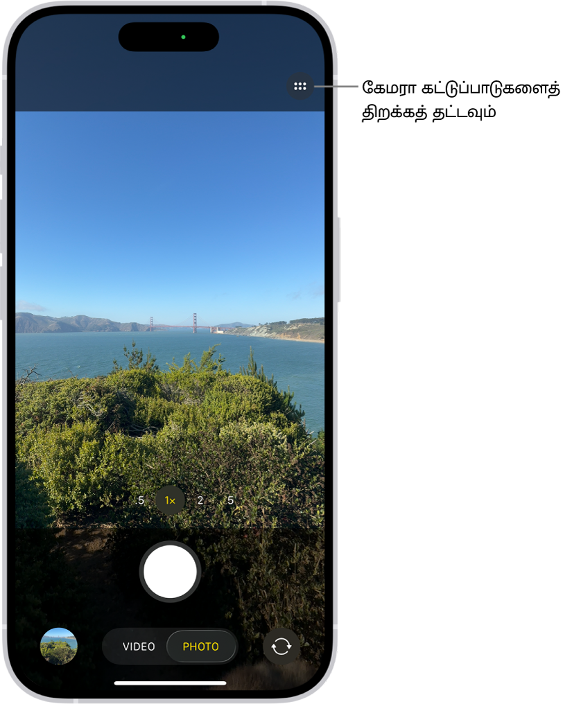 புகைப்படப் பயன்முறையில் கேமரா திறந்துள்ளது. மேல் வலது மூலையில் கேமரா கட்டுப்பாட்டுகள் பட்டன் உள்ளது. “புகைப்படம் மற்றும் வீடியோ வியூவர்” பட்டன் கீழ் இடது மூலையில் உள்ளது. “படமெடு” பட்டன் கீழ் மையத்திலும், “கேமரா தேர்வி - பின்பக்க கேமரா” பட்டன் கீழ்-வலது மூலையிலும் உள்ளது.