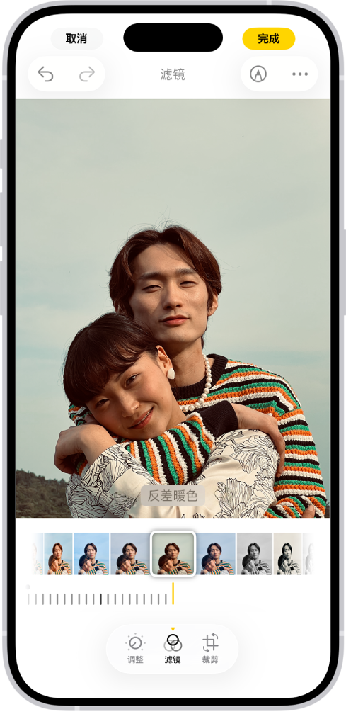 照片在中央的“编辑”屏幕。屏幕底部从左到右依次为“调整”、“滤镜”、“裁剪”和“消除”按钮。“滤镜”按钮已选中。照片下方是不同的滤镜选项。“反差暖色”已选中，还显示一个用于调整滤镜强度的滑块。屏幕左上角是“取消”按钮，右上角是“完成”按钮。