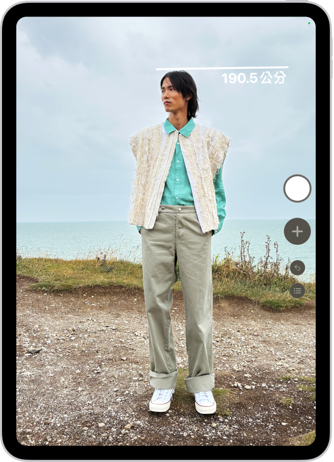 在「測距儀」App 中測量一個人的身高,身高測量結果顯示在此人頭頂上方。畫面右下角附近有可用來拍下量測結果的「拍照」按鈕。畫面頂部顯示綠色的「相機使用中」指示器。