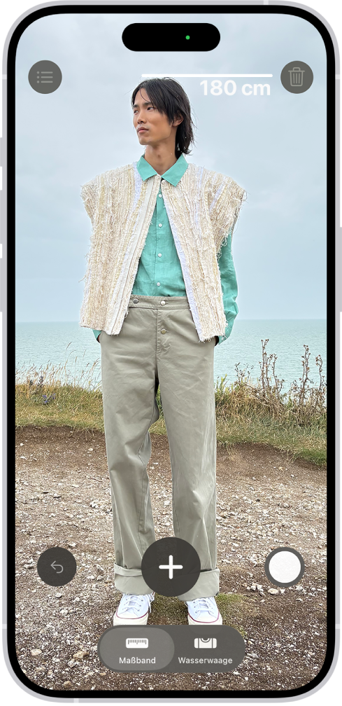 Die Größe einer Person wird in der App „Maßband“ gemessen. Über der Person wird die Größenmessung angezeigt. Die Taste „Bild aufnehmen“ befindet sich unten rechts, damit du ein Bild der Messung aufnehmen kannst. Die grüne Anzeige für „Kamera in Verwendung“ wird oben angezeigt.