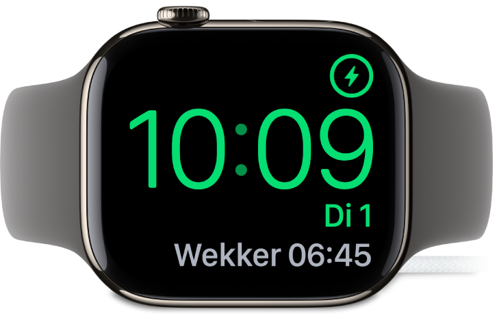 Een Apple Watch die op zijn kant ligt en is aangesloten op de oplader. Rechtsbovenin bevindt zich het oplaadsymbool en daaronder staan de actuele tijd en de tijd van de volgende wekker.