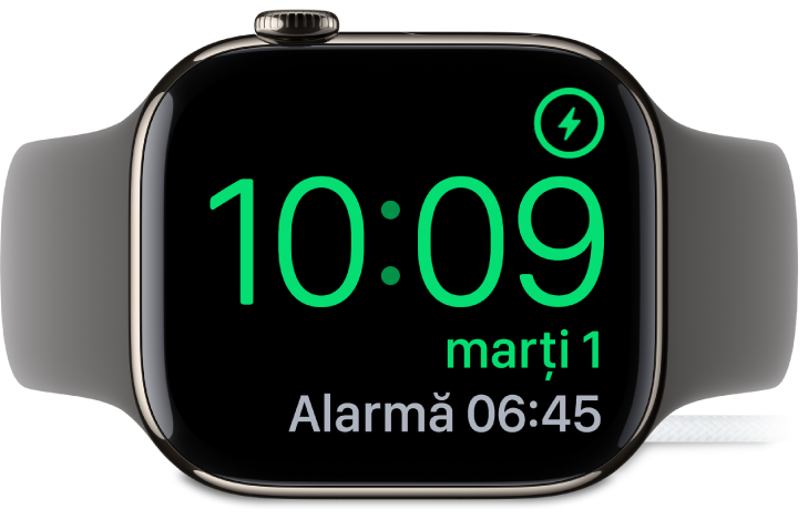 Un Apple Watch așezat pe muchie și conectat la încărcător, pe ecran fiind afișat simbolul de încărcare în colțul din dreapta sus, ora actuală dedesubt și ora alarmei următoare.