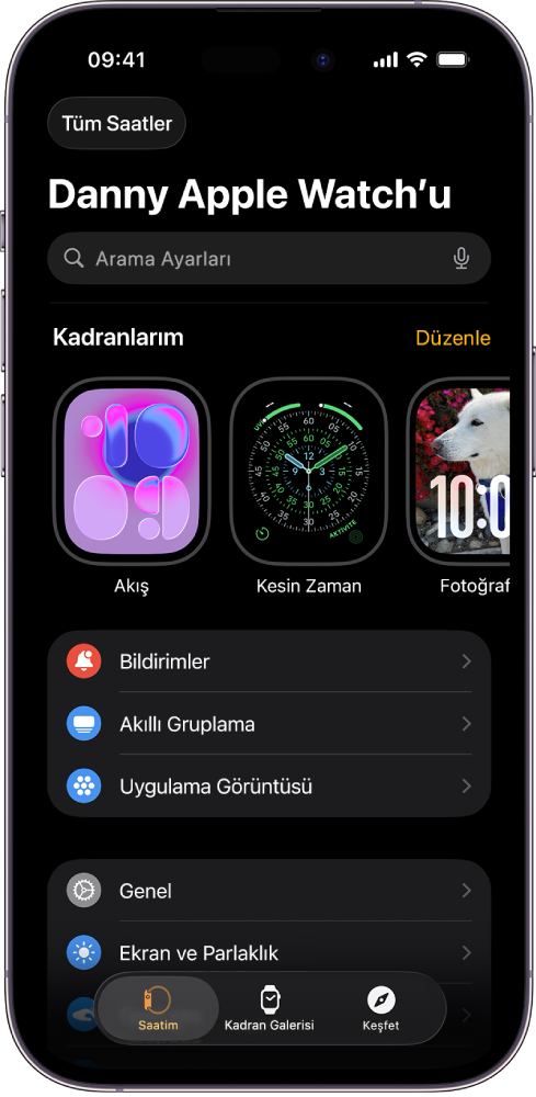 Üst tarafta saat kadranlarını ve altta ayarları gösteren Saatim ekranı açık olarak iPhone’daki Apple Watch uygulaması. Apple Watch uygulaması ekranının en altında üç sekme var: Soldaki sekme Apple Watch ayarlarını yapmak için gittiğiniz Saatim; yanındaki, kullanılabilir saat kadranlarını ve komplikasyonları keşfedebileceğiniz Kadran Galerisi ve diğeri, Apple Watch hakkında daha fazla bilgi edinebileceğiniz bir yer olan Keşfet sekmesi.